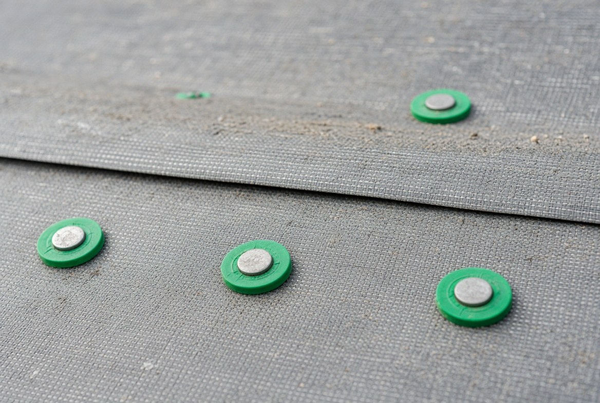Close-up of green plastic cap nails through synthetic underlayment